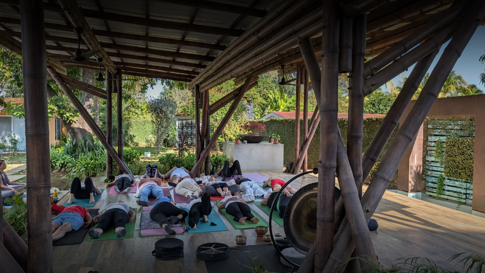 Esta imagen muestra un grupo de personas participando en una sesión de baño de sonido y meditación al aire libre en una terraza