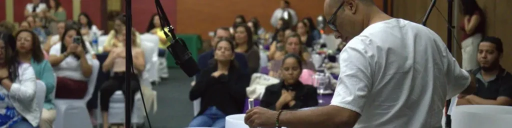 Juan Domínguez facilitando un baño de sonido grupal en vivo para una audiencia sentada en un salón de conferencias en Nicaragua. Se le ve tocando instrumentos de cristal mientras los participantes experimentan meditación y relajación profunda en un entorno corporativo.