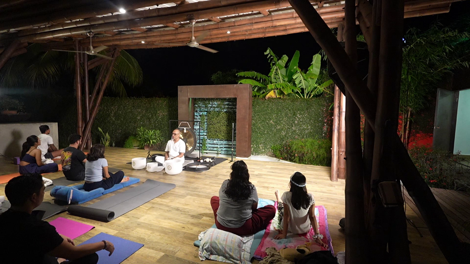Esta imagen muestra un grupo de personas participando en una sesión de baño de sonido y meditación al aire libre en una terraza